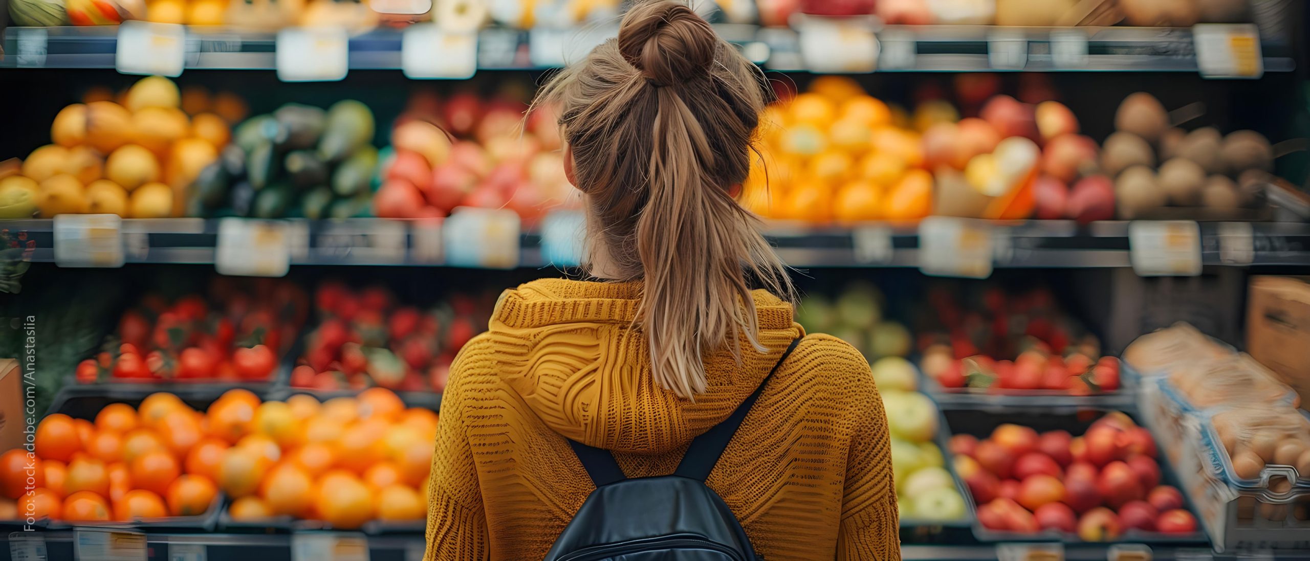 Eine Frau steht vor vollen Regalen in der Obstabteilung eines Supermarktes.