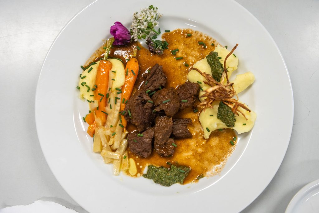 Geschmortes Fleisch liegt liebevoll angerichtet auf einem weißen Teller